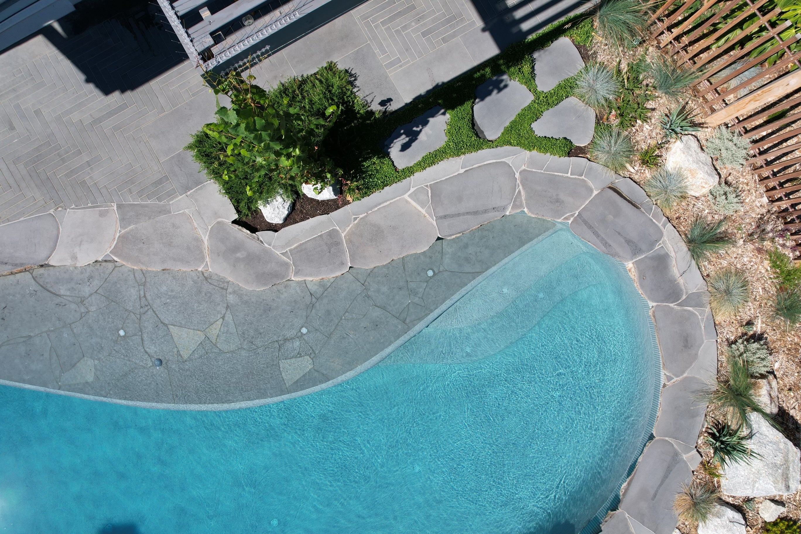 Aerial view of a swimming pool with stone coping and surrounding garden.