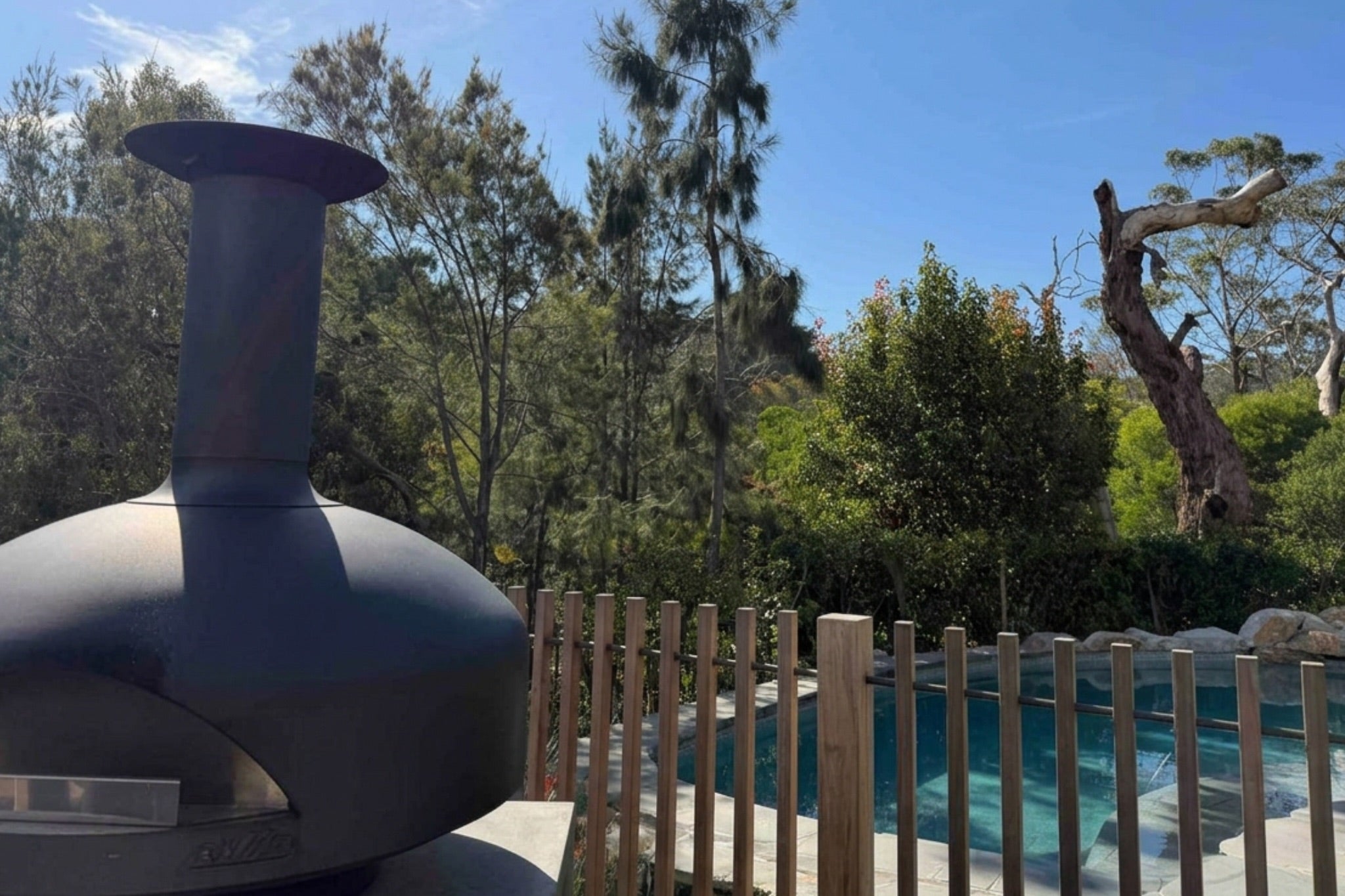 Outdoor pizza oven by a pool with trees in the background